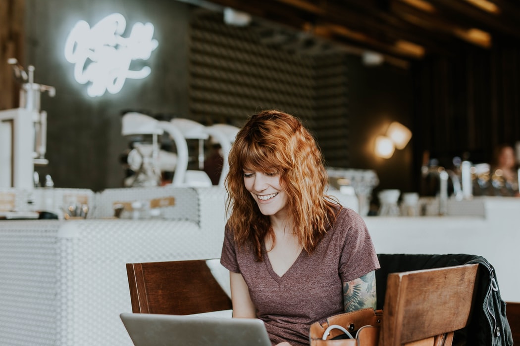 femme devant son ordinateur dans un restaurant qui sourit