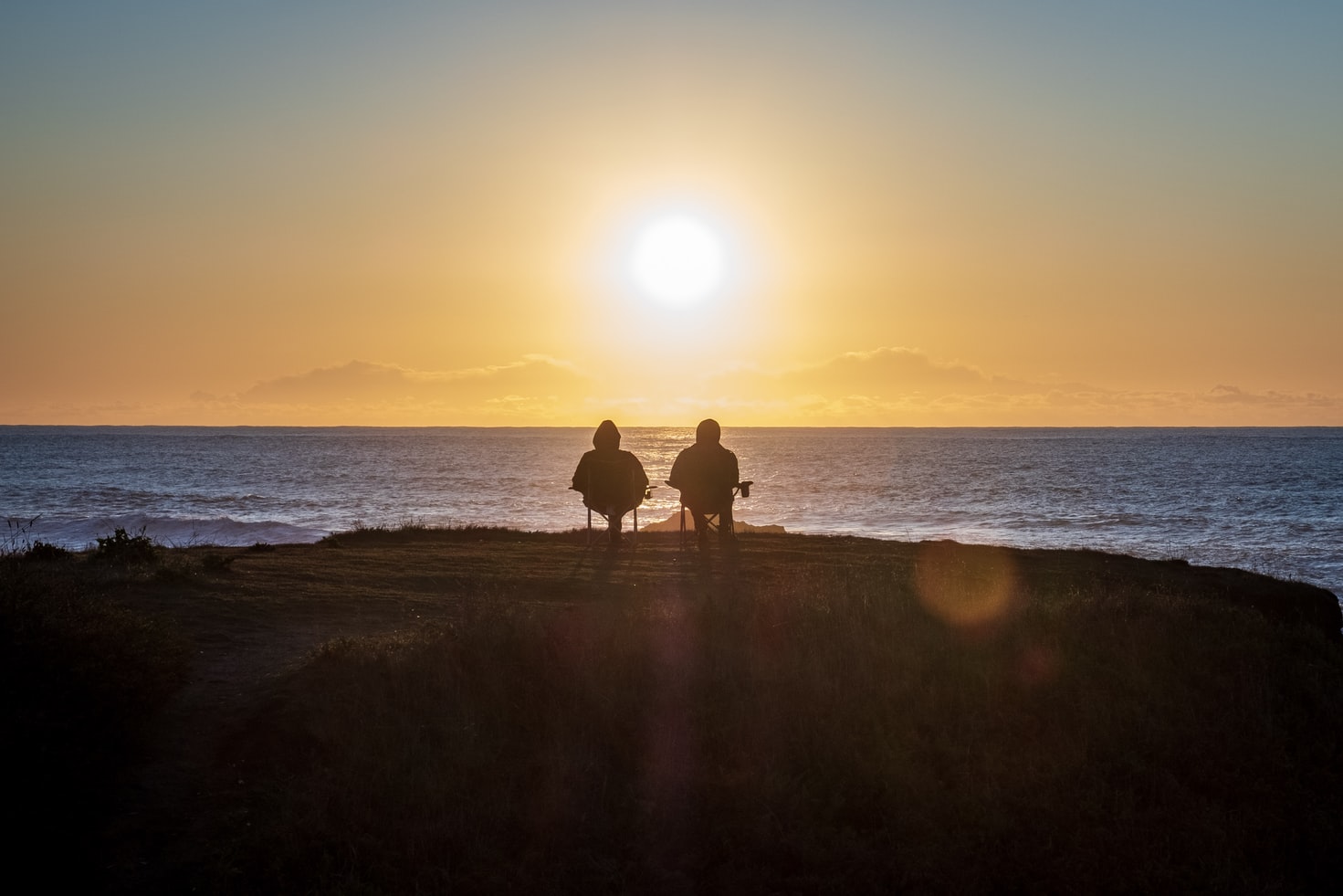 deux personnes assises de dos devant l'océan et le couché du soleil